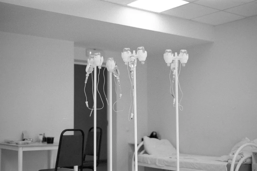 Mehrere Infusionsständer neben einem Krankenbett in einem stillen Klinikzimmer