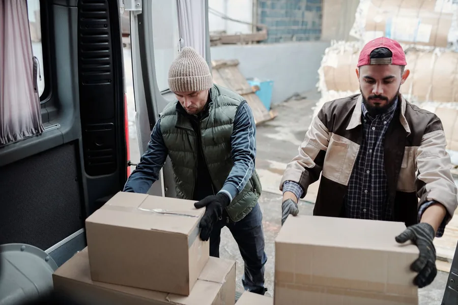 Zwei Versandmitarbeiter verladen Kartons in einen Lieferwagen.