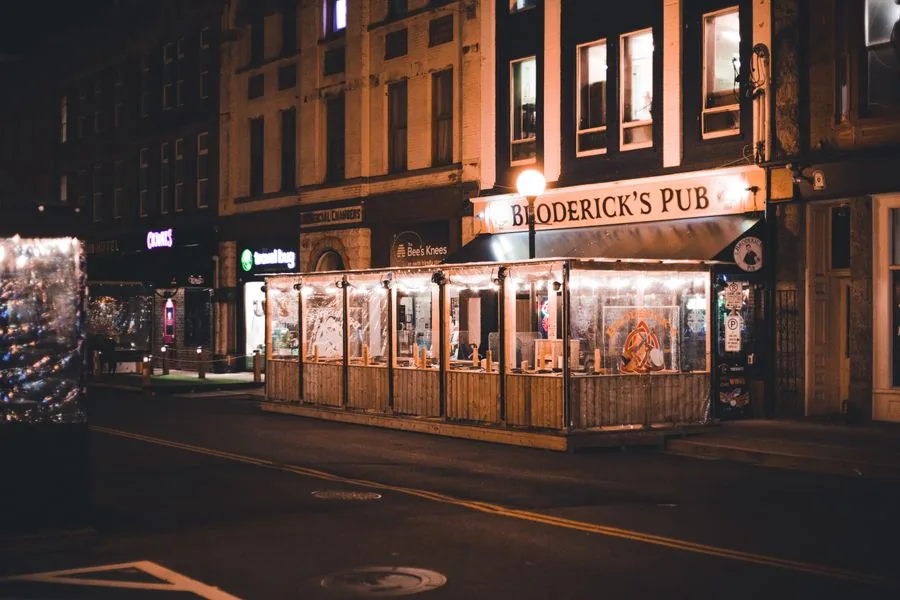 Außenansicht einer Bar mit beleuchtetem Eingang an einer nächtlichen Straße mit Gehweg und Straßenlaterne