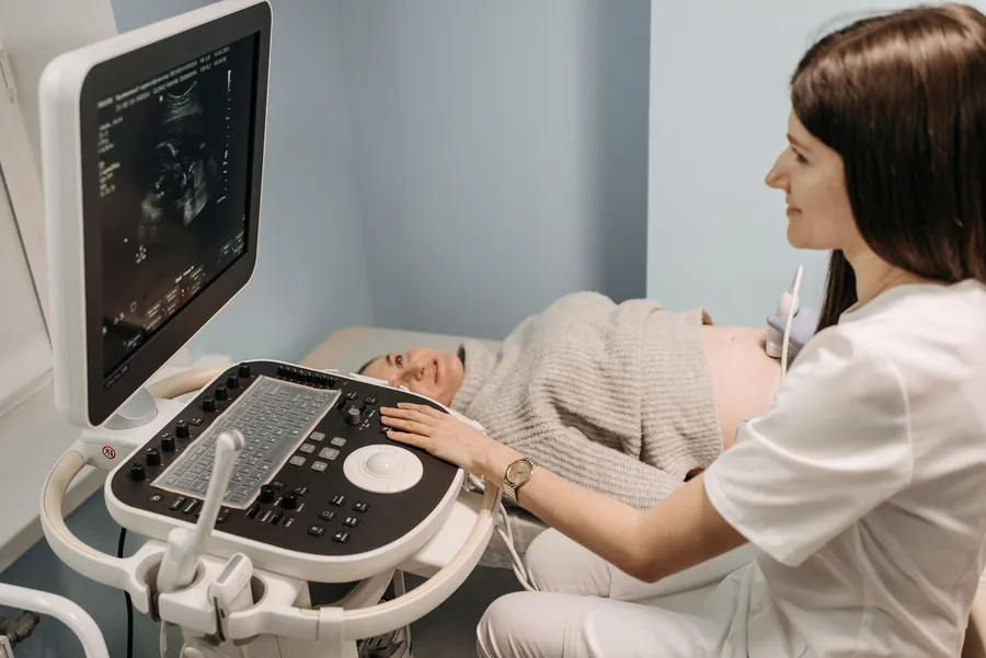 Ärztin führt eine Ultraschalluntersuchung an einer schwangeren Patientin durch, der Monitor zeigt das Bild