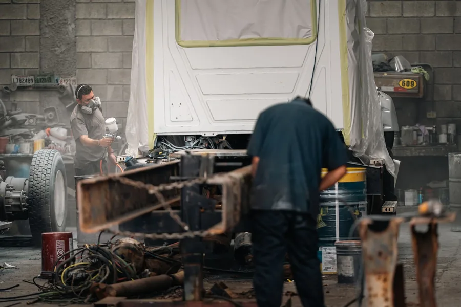 Zwei Arbeiter in Schutzkleidung lackieren ein Fahrzeug in einer Lackierkabine
