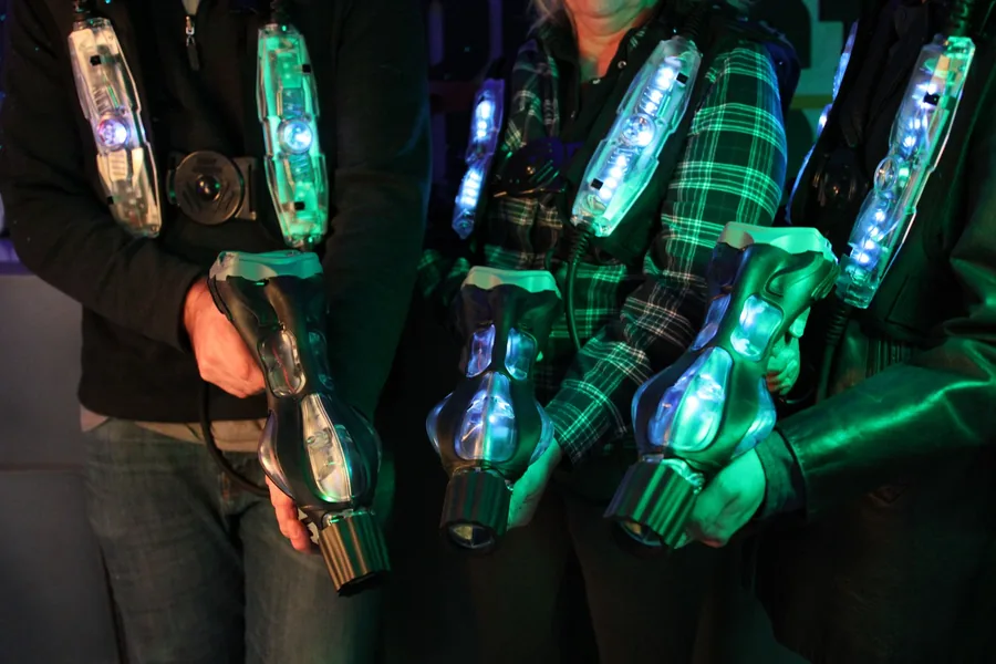 Spieler mit leuchtenden Lasertag-Westen und Laserpistolen im Neonlicht