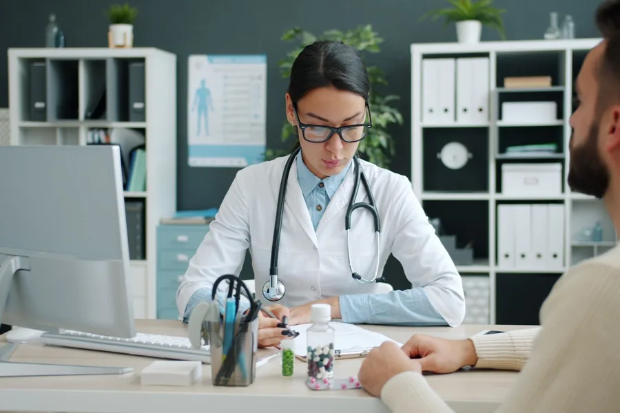 Eine Ärztin sitzt am Tisch einem Patienten gegenüber und erklärt ihm ein Aufklärungsformular