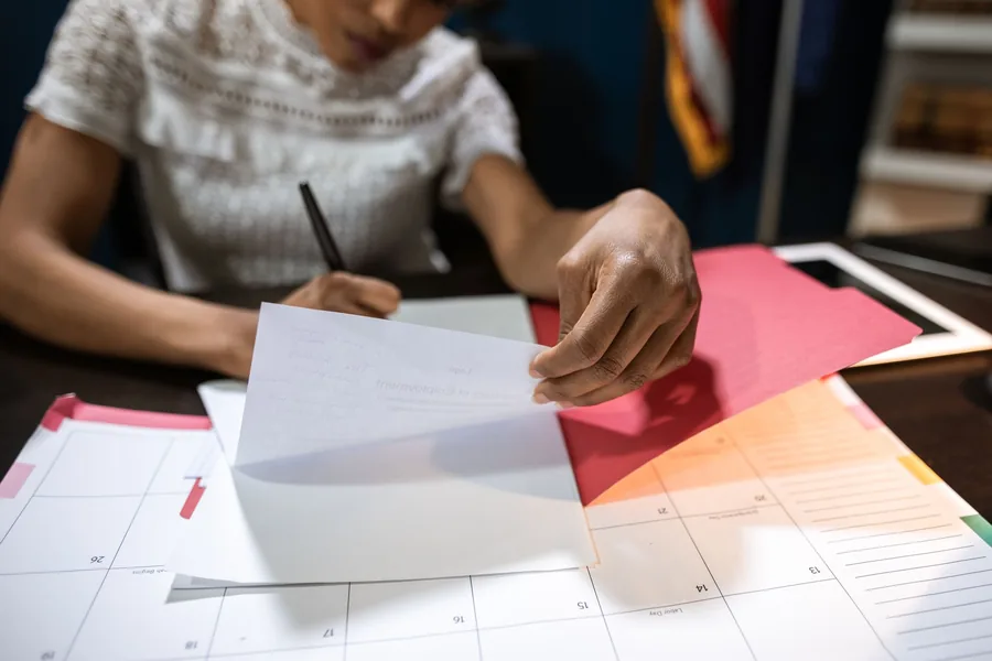 Person unterschreibt ein Schreiben neben einem Kalender auf dem Schreibtisch