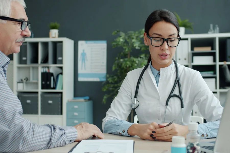 Ärztin bespricht mit einem älteren Patienten ein Dokument im Sprechzimmer