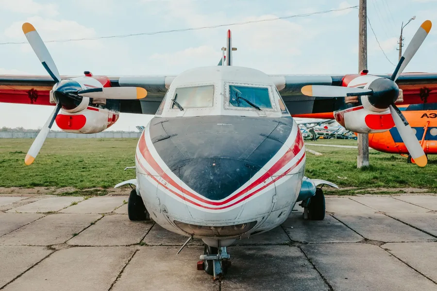 Kleines zweimotoriges Propellerflugzeug steht frontal auf einem Betonvorfeld, dahinter Wiese und weitere Maschinen