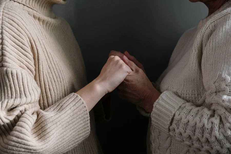 Eine Tochter hält die Hand ihrer bettlägerigen Mutter, Nahaufnahme der ineinandergelegten Hände