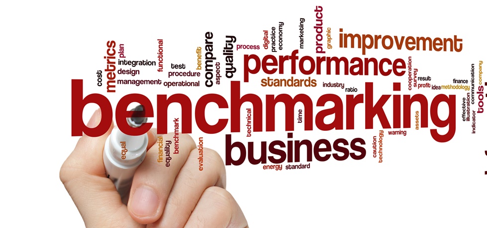 hand with pen writing "benchmarking" and associated words