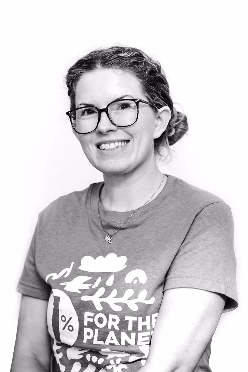 Smiling woman with glasses and hair in bun wearing a '1% For The Planet' t-shirt.