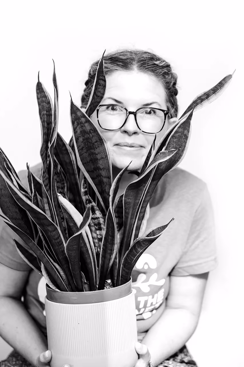 Person with glasses holding a tall potted snake plant with long striped leaves.