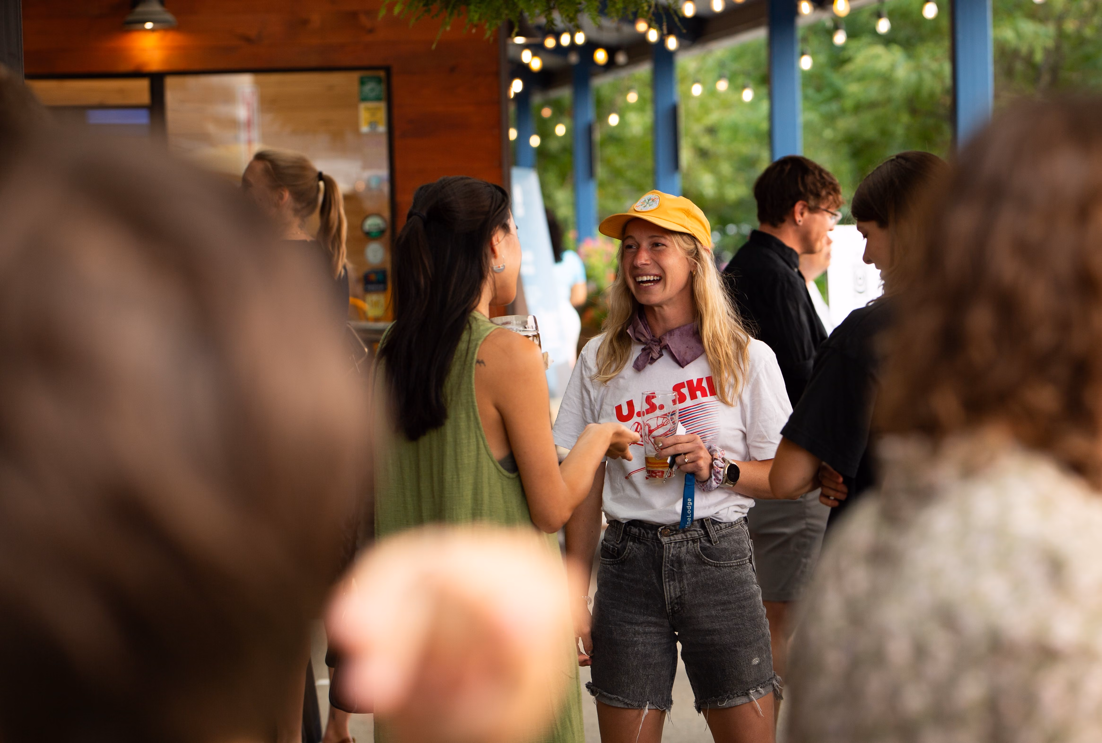 Two women smiling and talking at an outdoor social gathering with string lights overhead.