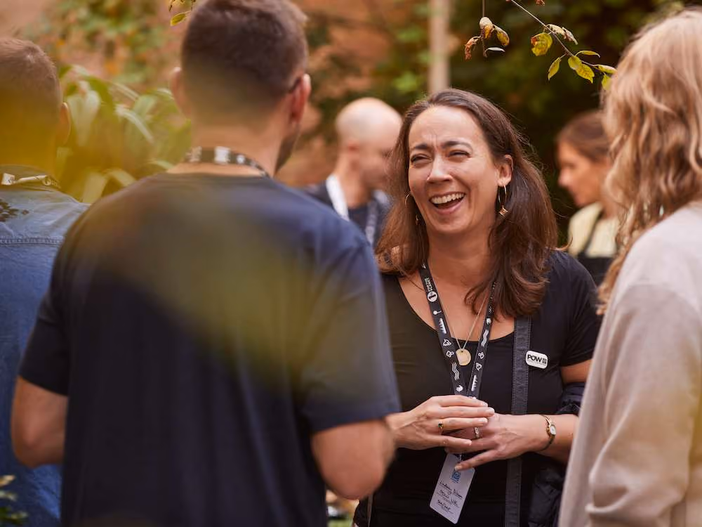 Smiling woman with badge chatting with others outdoors in a lively social gathering.