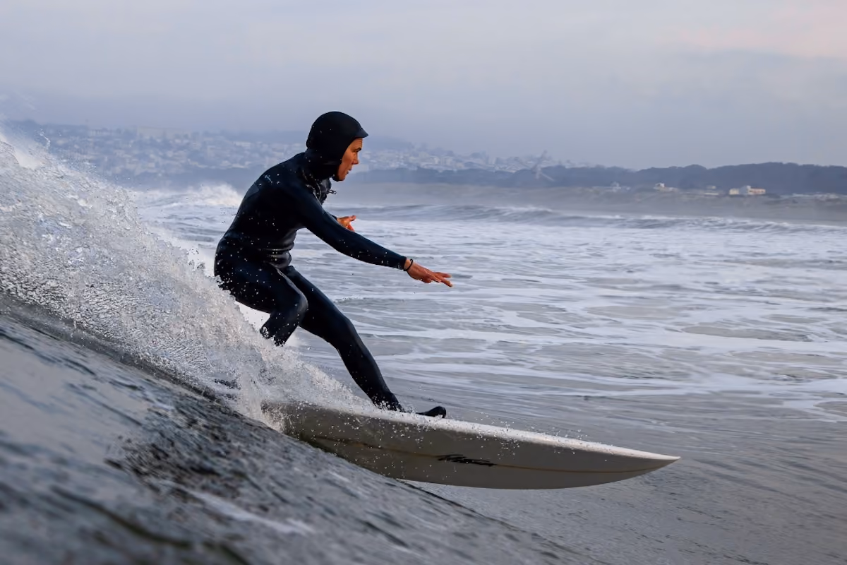 Surfer in a black wetsuit riding a wave on a white surfboard near a foggy coastline.