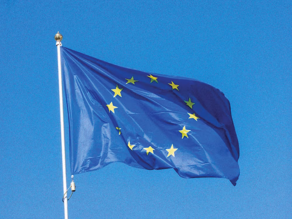 European Union flag with twelve yellow stars on a blue background waving against clear sky.