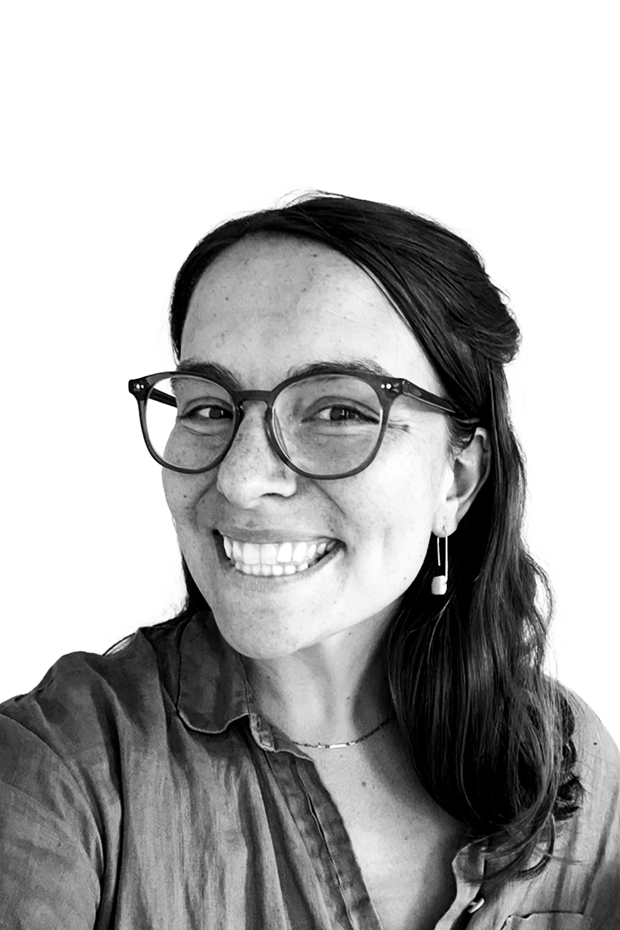 Smiling woman with glasses, long dark hair, wearing earrings and a collared shirt, against a white background.