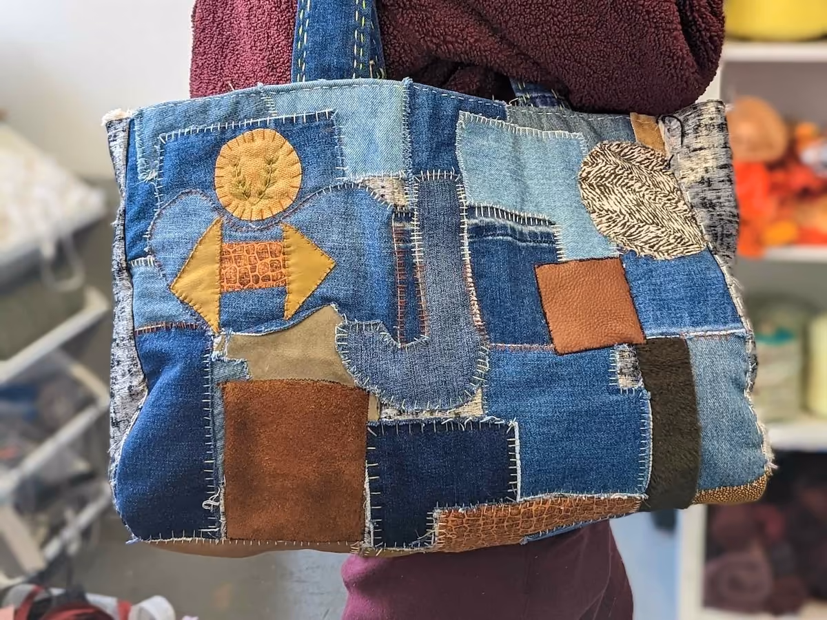 Patchwork tote bag made of various denim and leather fabric pieces stitched together.