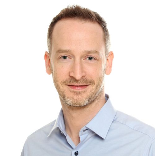 Portraitfoto von Jonas. Er trägt ein hellblaues Hemd. Er hat kurze dunkelblonde Haare. Er lächelt in die Kamera.