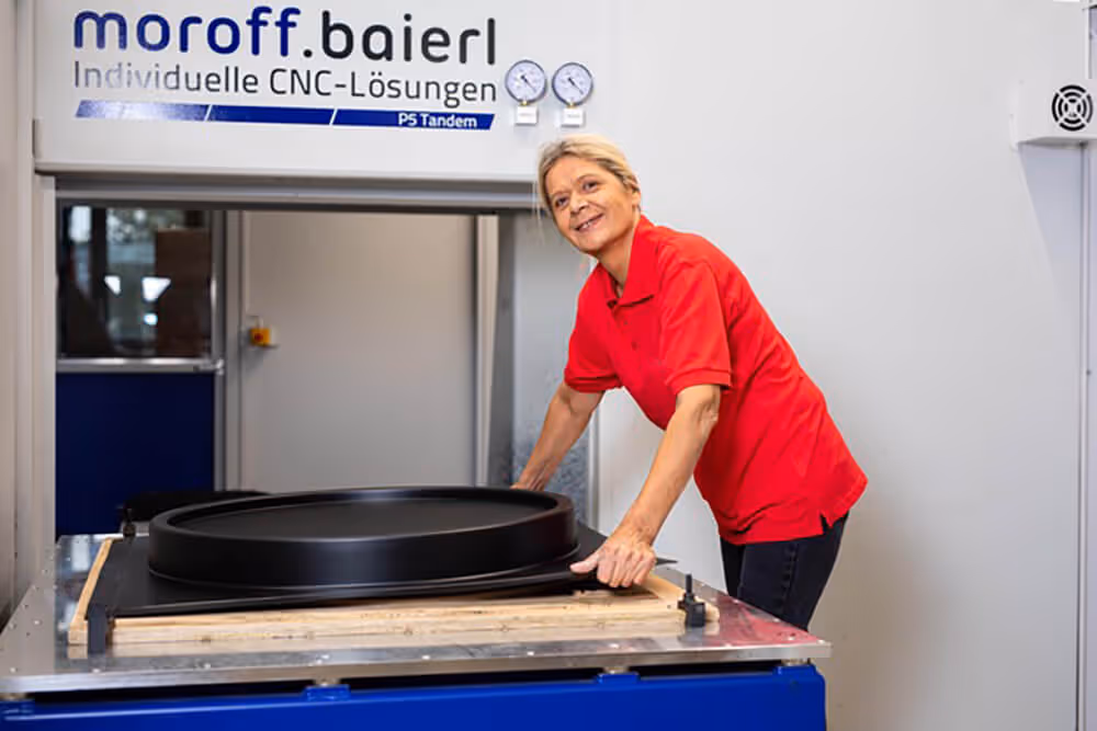 Eine Fachkraft, die lächelt und im integrativen Betrieb eine perfekt gepresste Kunststoffform aus der Produktionsanlage entnimmt.