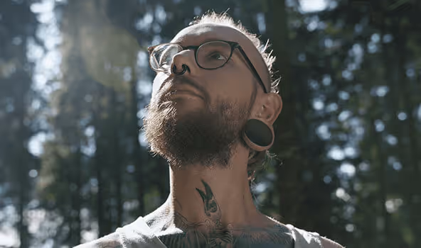 Tobias, Tischler in einem integrativen Betrieb, blickt nach oben in die Bäume eines Waldes.
