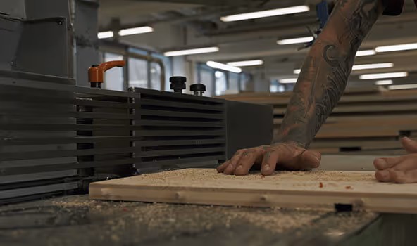 Die Hände von Tobias, Tischler in einem integrativen Betrieb, während sie ein Werkstück an der Hobelmaschine bearbeiten.