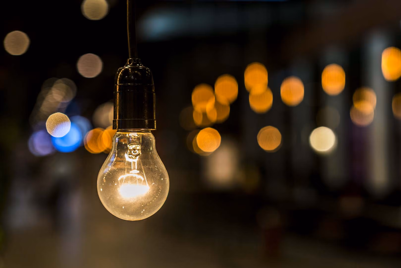 Close-up of a glowing hanging light bulb with blurred warm lights in the background.