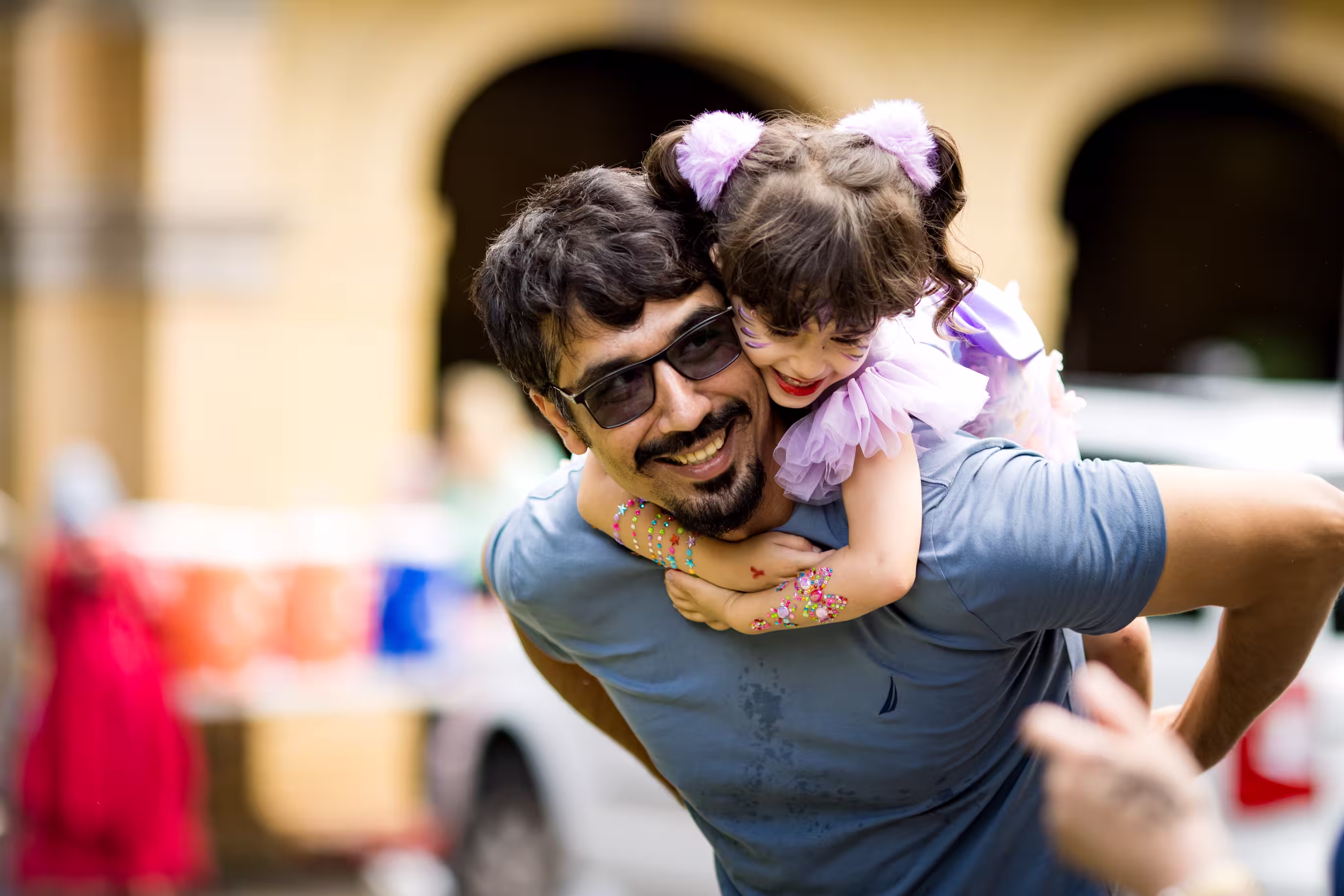 A smiling father carries his young, bedazzled daughter on his back.