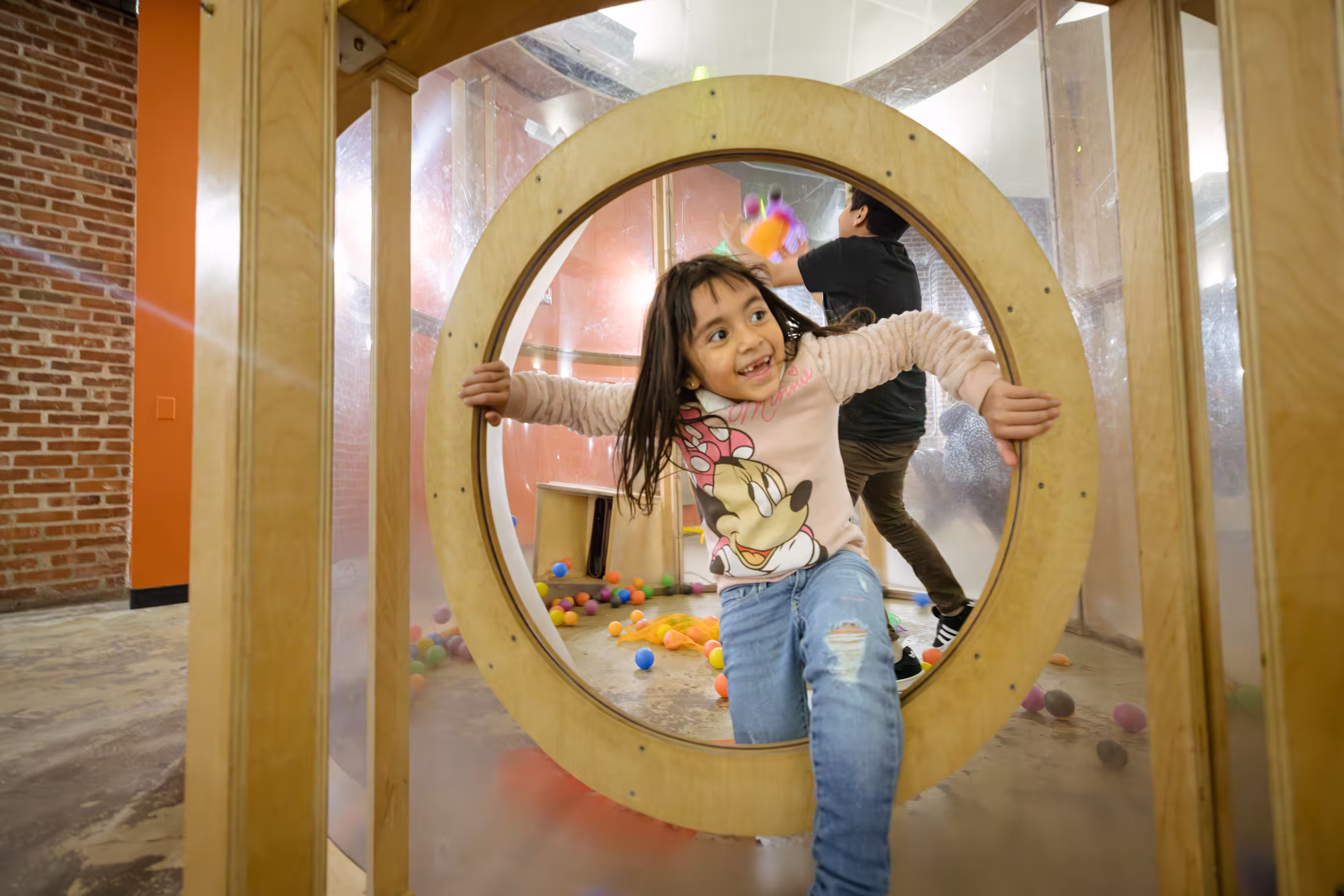 A young girl is smiling while climbing through a circular opening in a play place.