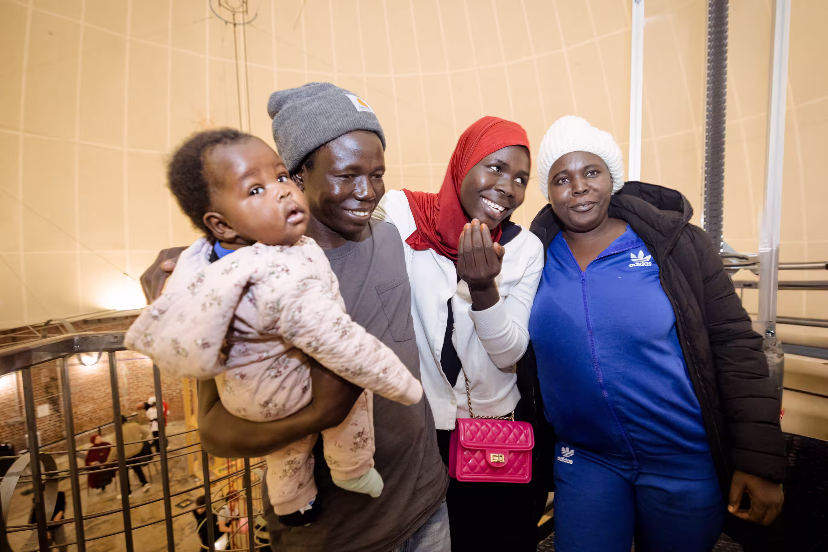 Three adults and a baby stand together for a picture, smiling and laughing.
