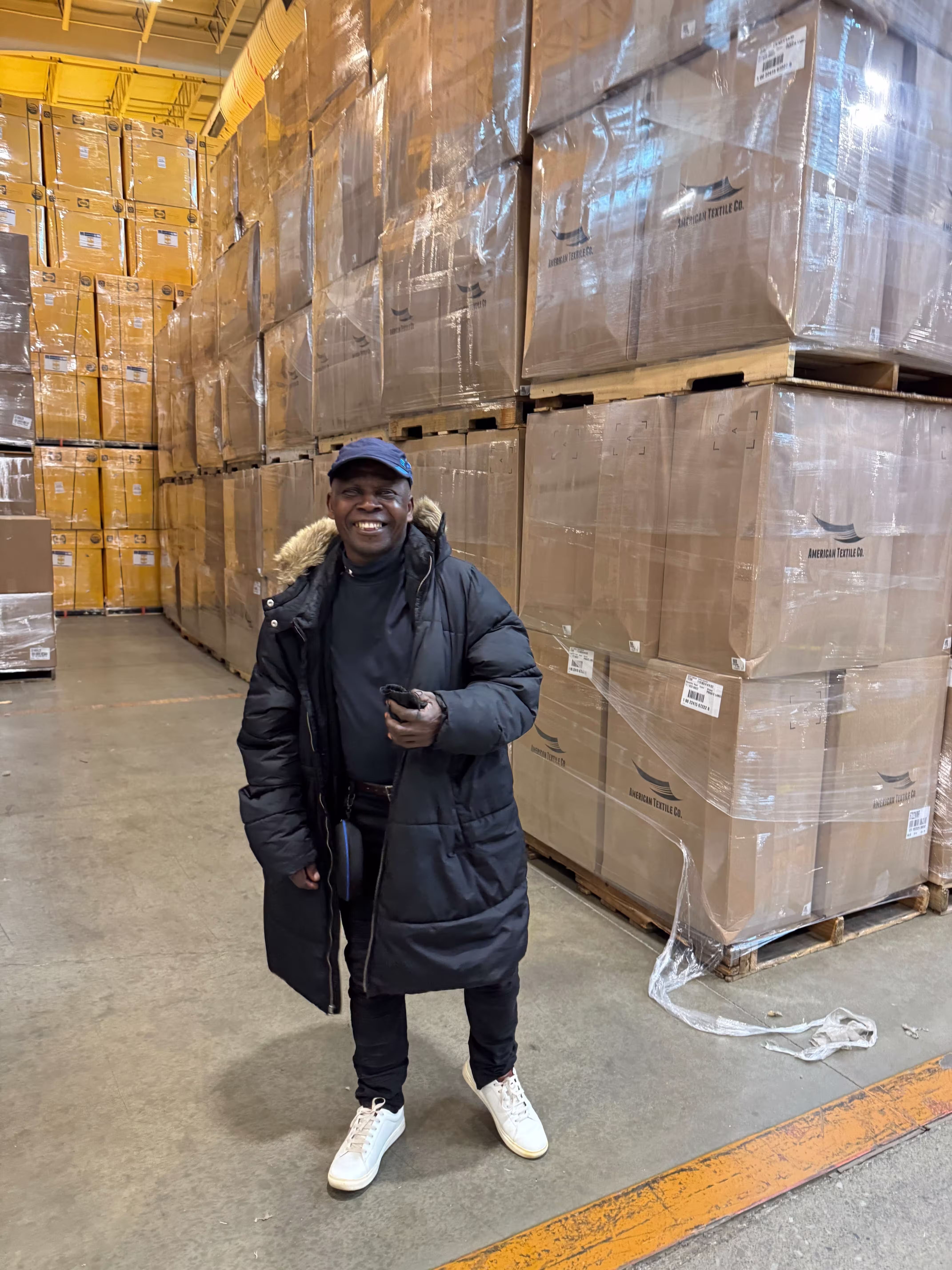 A man smiling in front of stacked pallets of cardboard boxes.