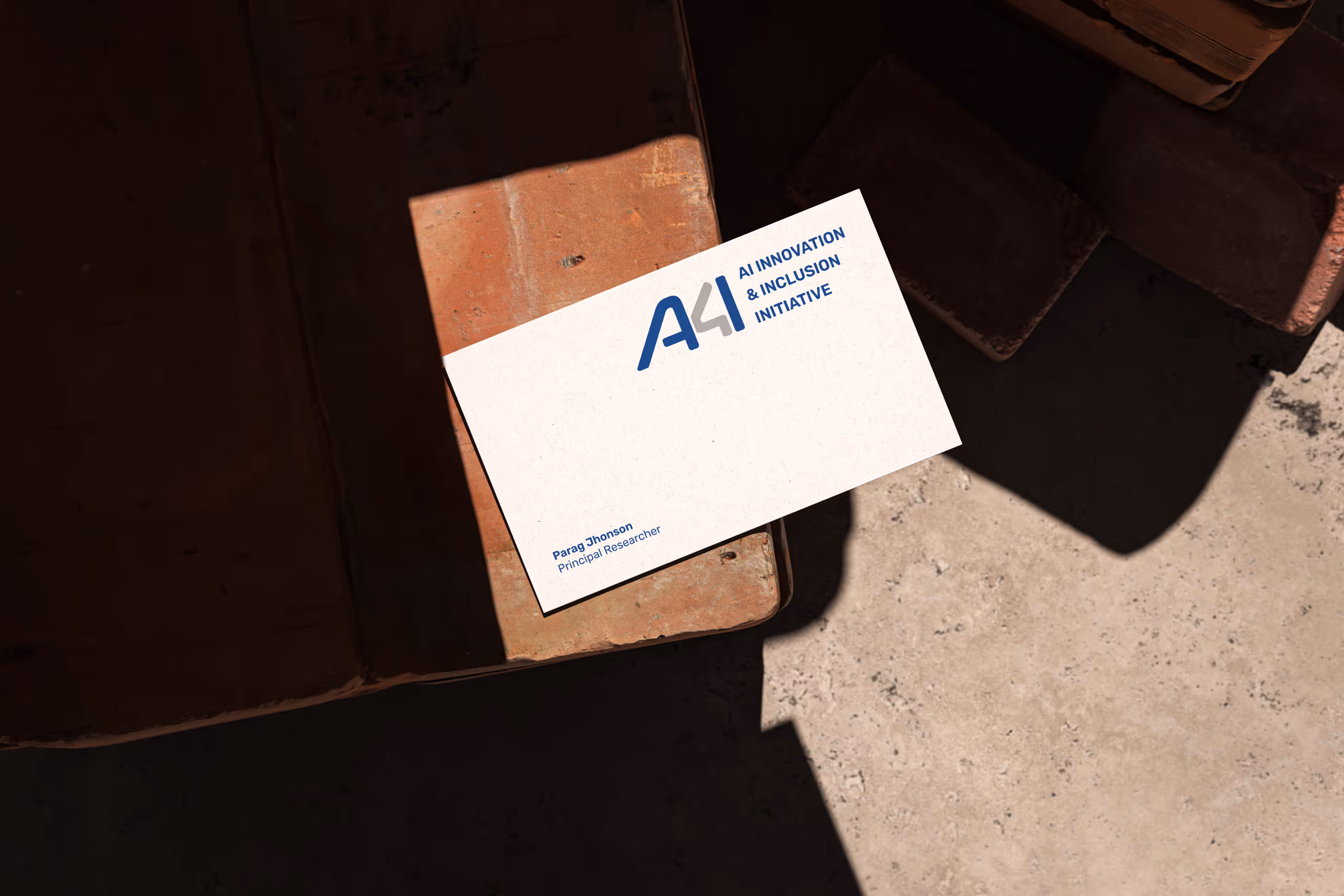 Business card for Parag Jhonson, Principal Researcher at AI Innovation & Inclusion Initiative, placed on a brick surface with shadows.
