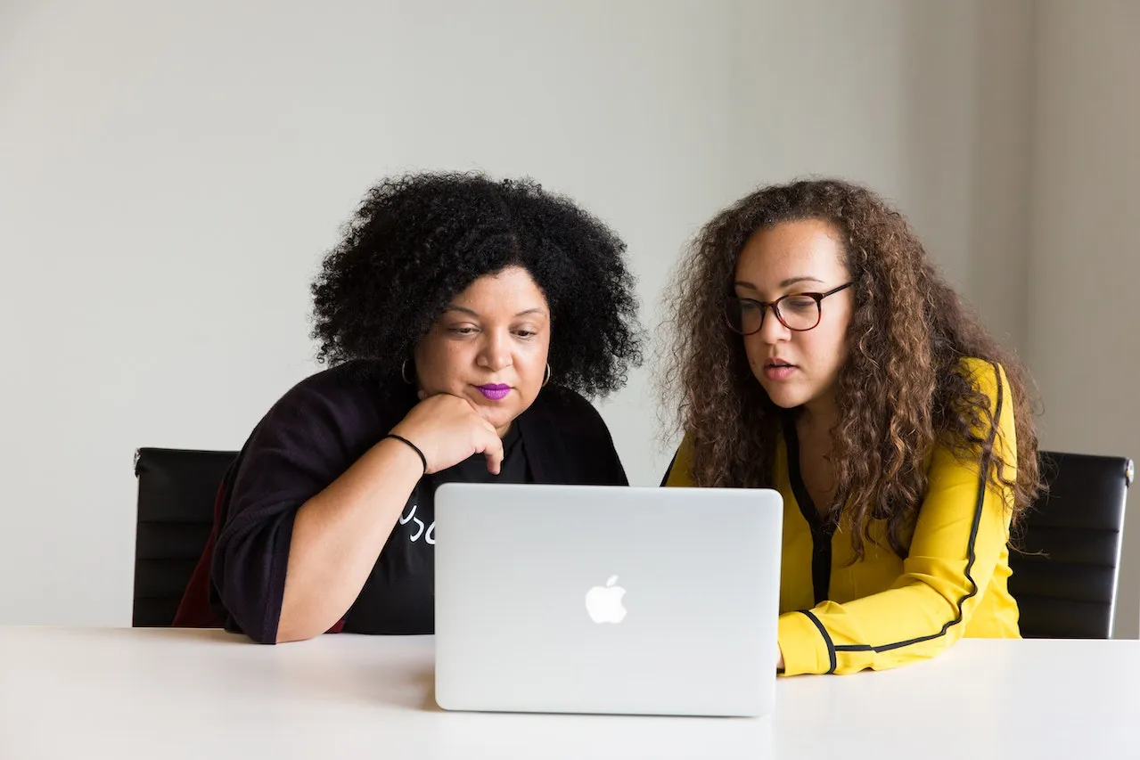 Two ladies sit at a table looking at a computer