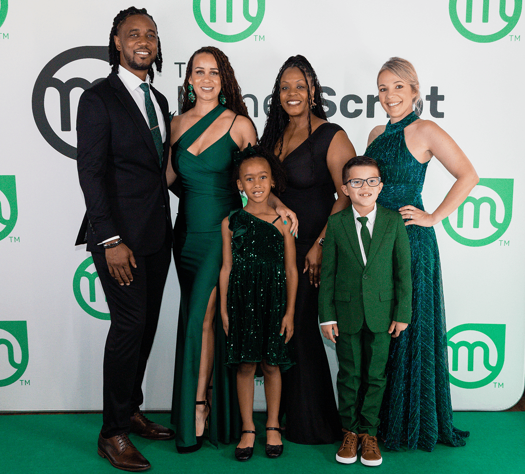 Five people dressed formally posing together, three women in black and green dresses, one woman in a pink dress, and one man in a black suit with a green tie.