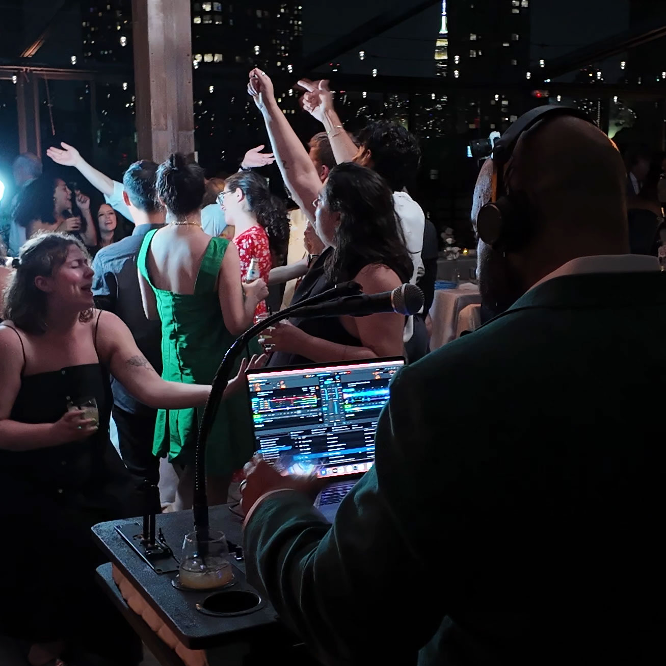 Box House Hotel, Brooklyn — Kenny Fiesta DJing with a packed dance floor; guests singing with the NYC skyline and Empire State Building in the background.