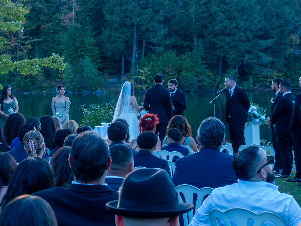 Lakeside ceremony — officiant and translator with couple, three bridesmaids and three groomsmen; clear ceremony audio and bilingual hosting.