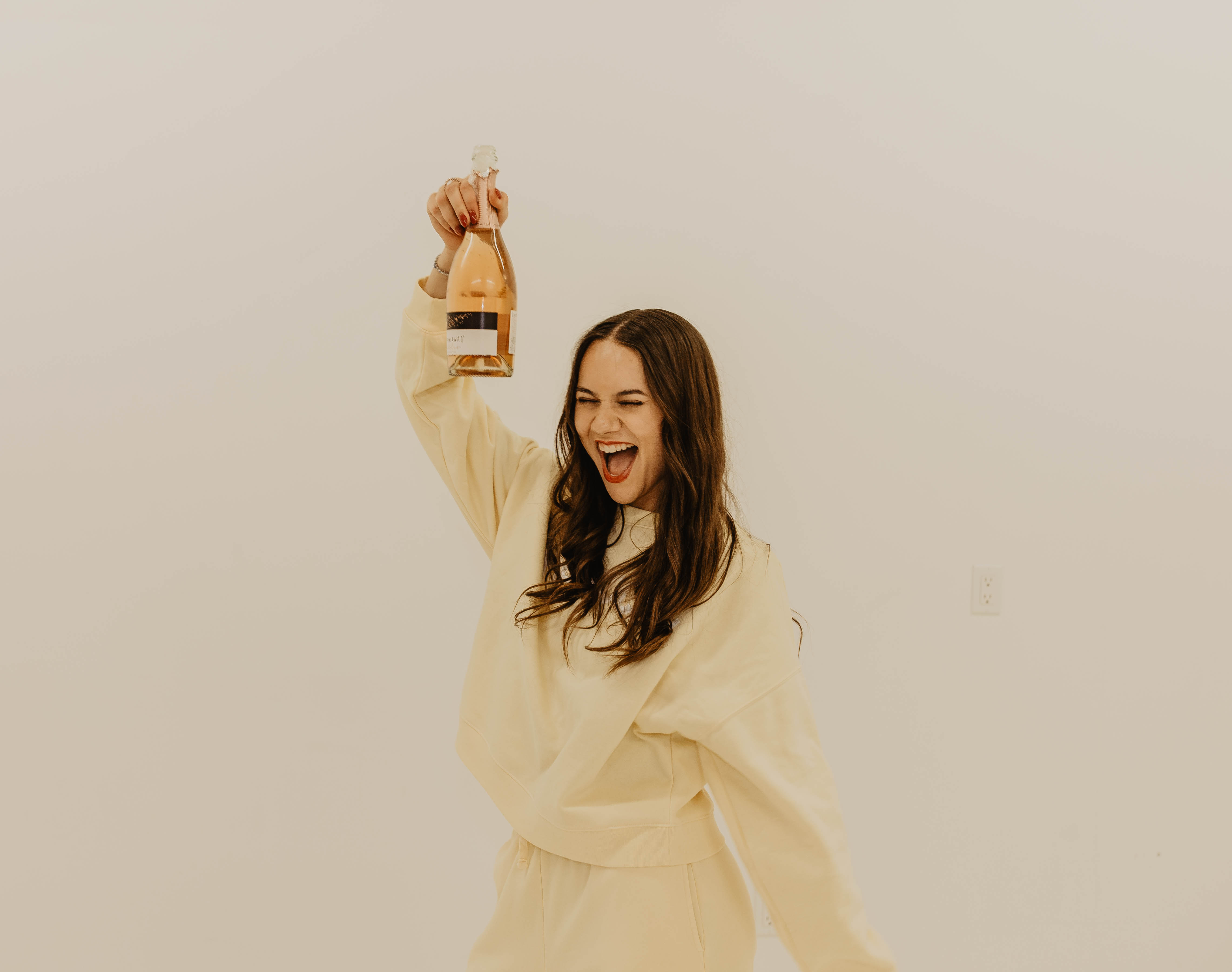 Maddie Thompson, founder of MAD Social Agency popping champagne wearing a yellow sweatsuit