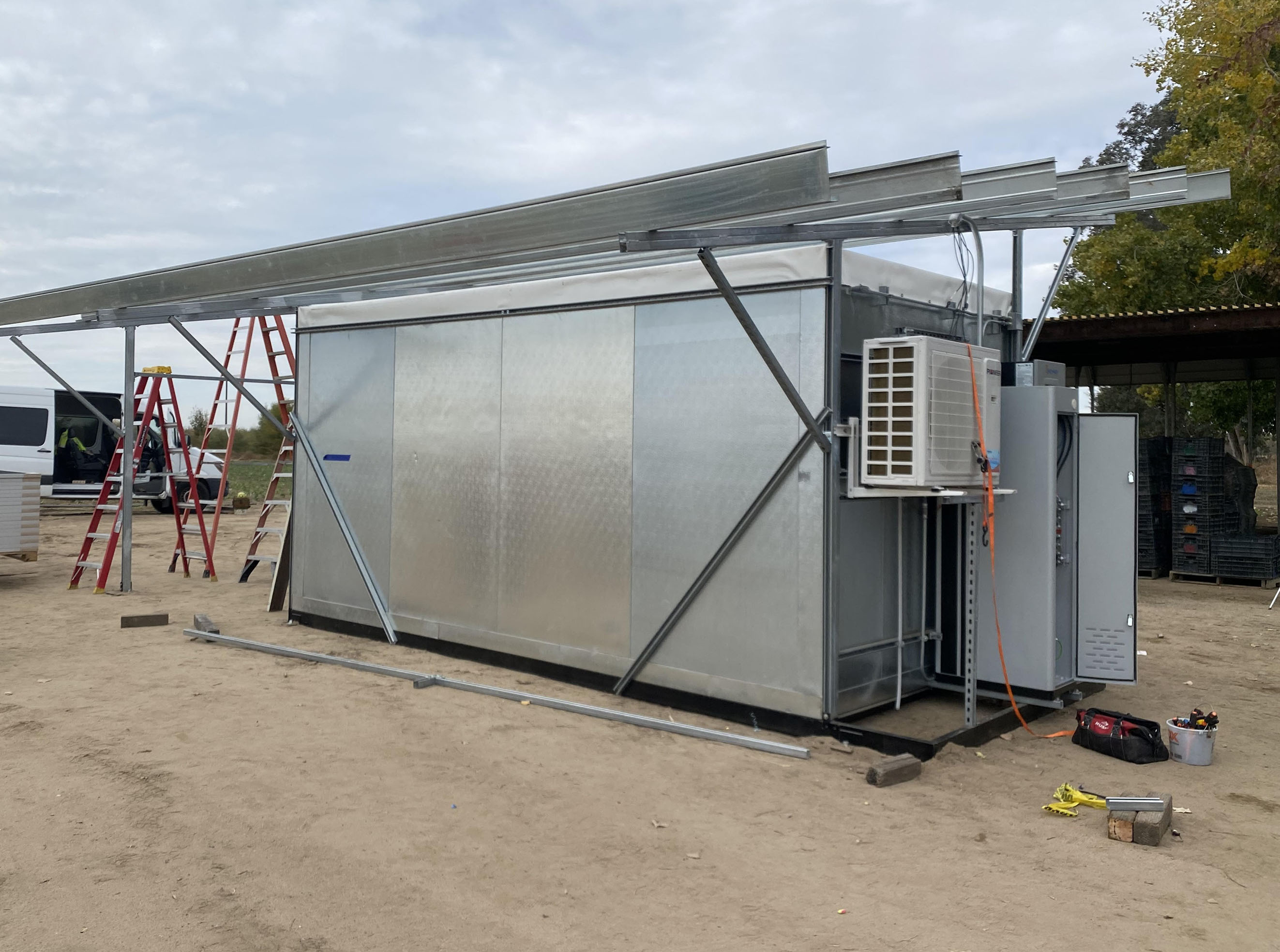 A solarfresco solar powered cooler stands in an unpaved part of a field 