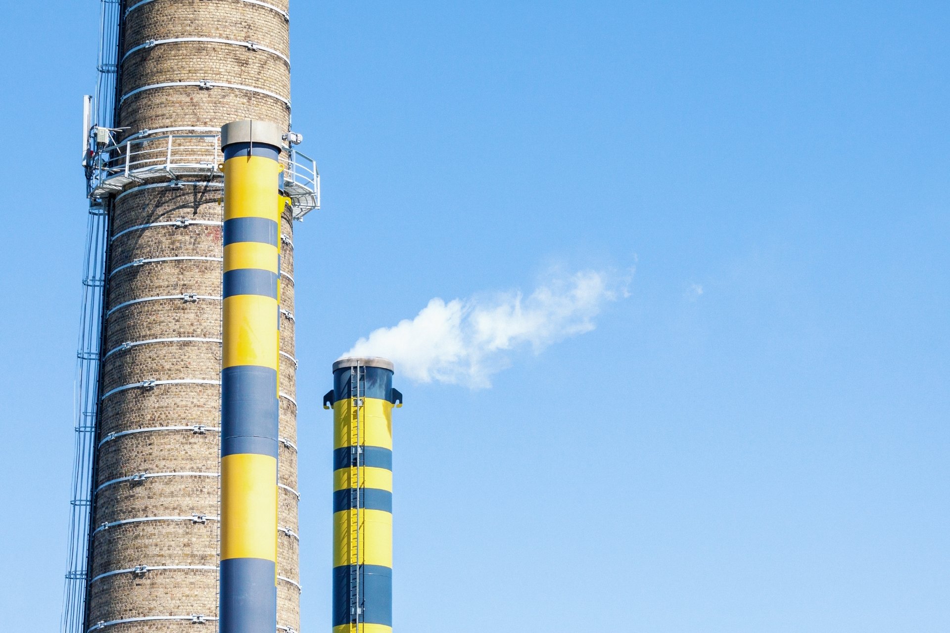 industrial chimneys emitting white smoke against a clear blue sky, emphasising the importance of site validation in monitoring emissions and ensuring environmental compliance.
