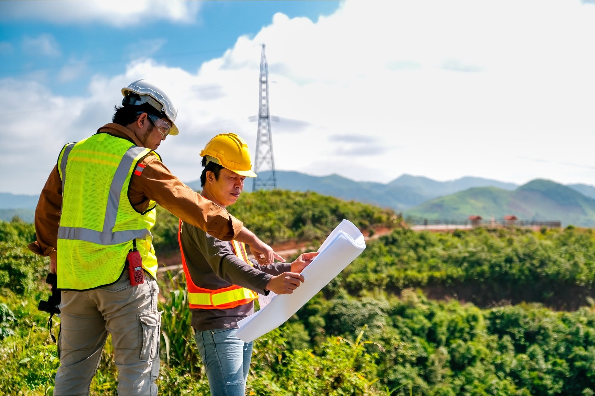 Two workers in safety gear review blueprints on a hillside, planning site development under an Environmental Management Plan (EMP).