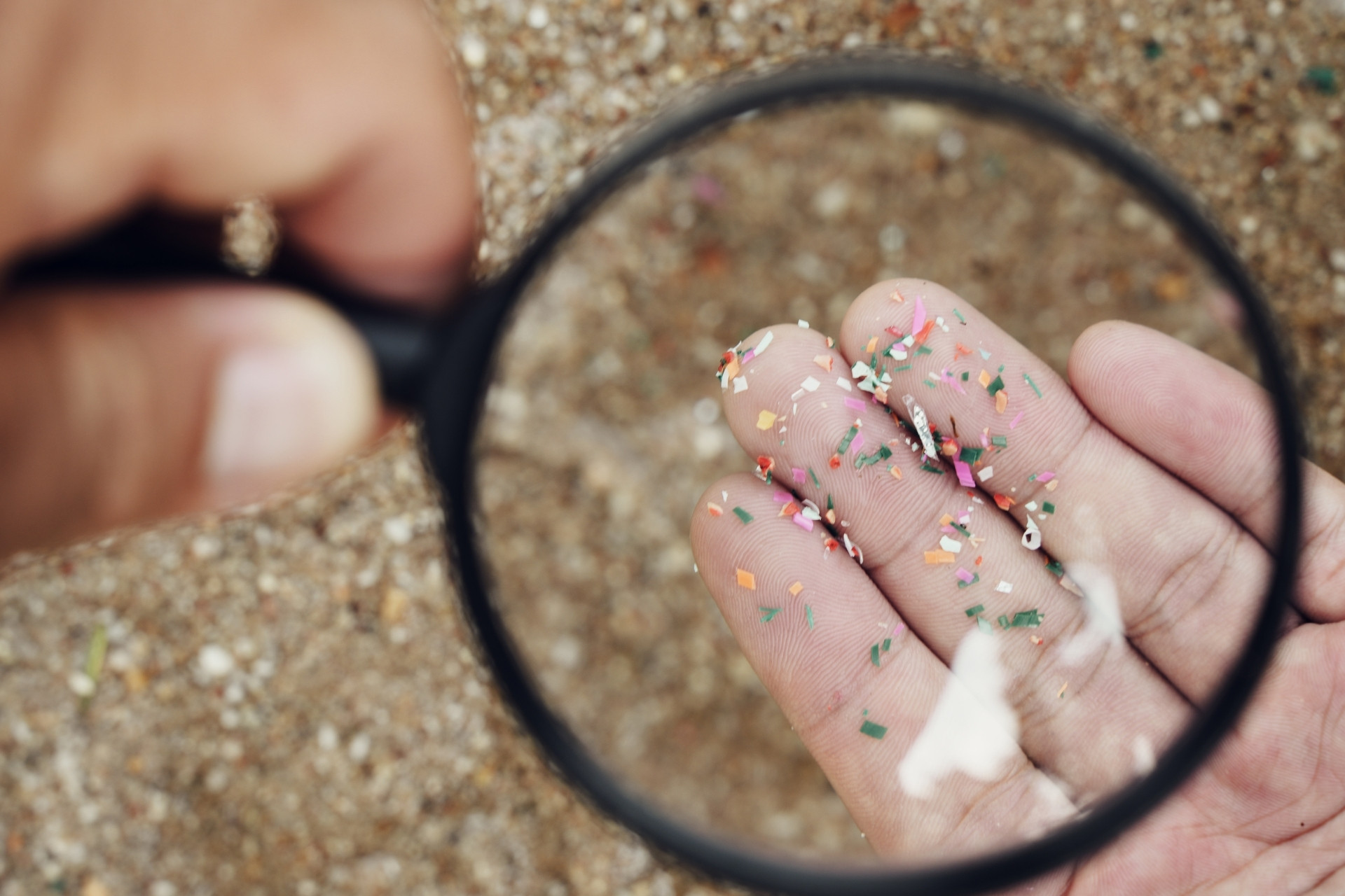 a hand holding a magnifying glass with microplastic