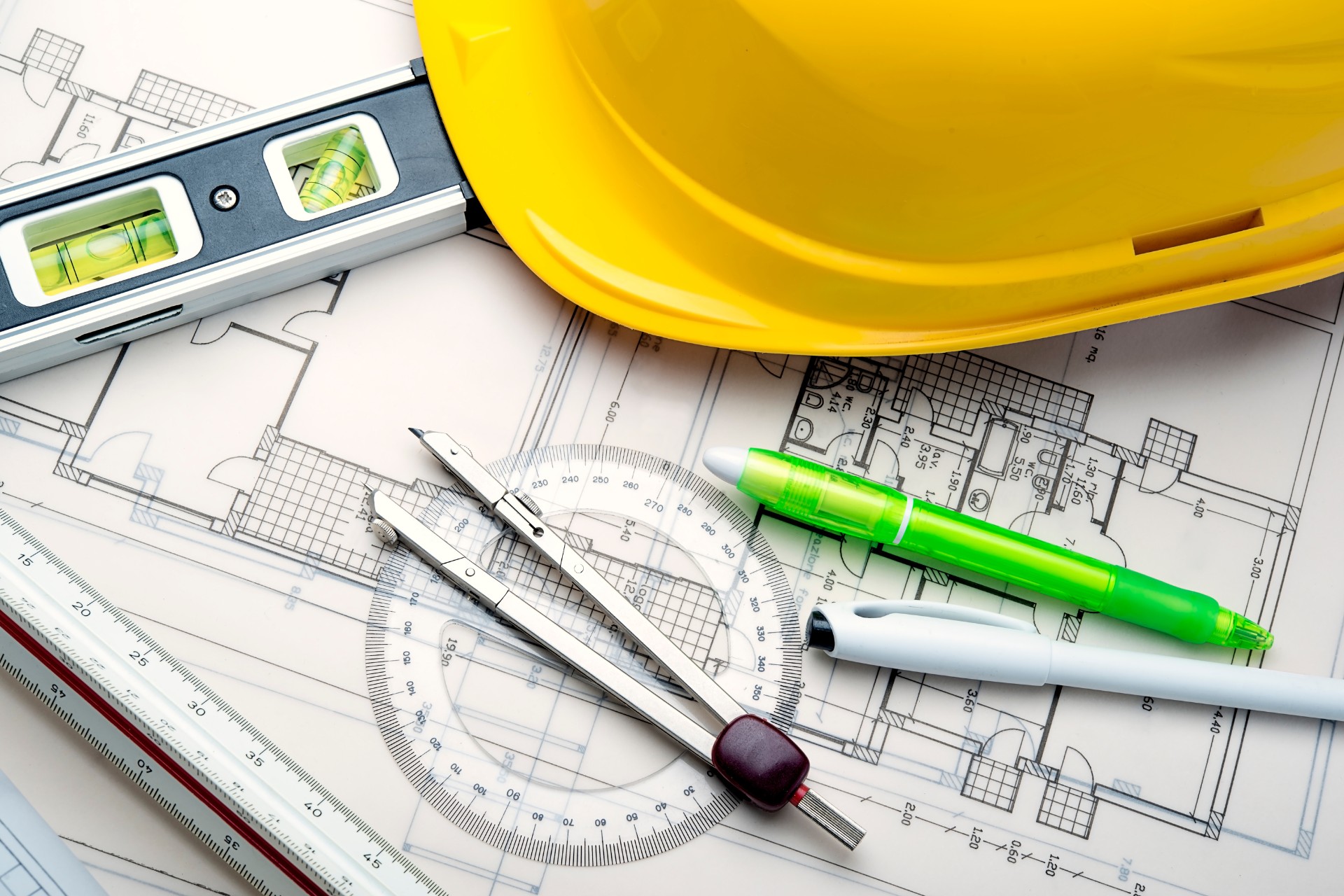 Close-up of architectural blueprints with drafting tools, a level, and a yellow hard hat, symbolizing planning and precision in developing a construction environmental management plan (CEMP).