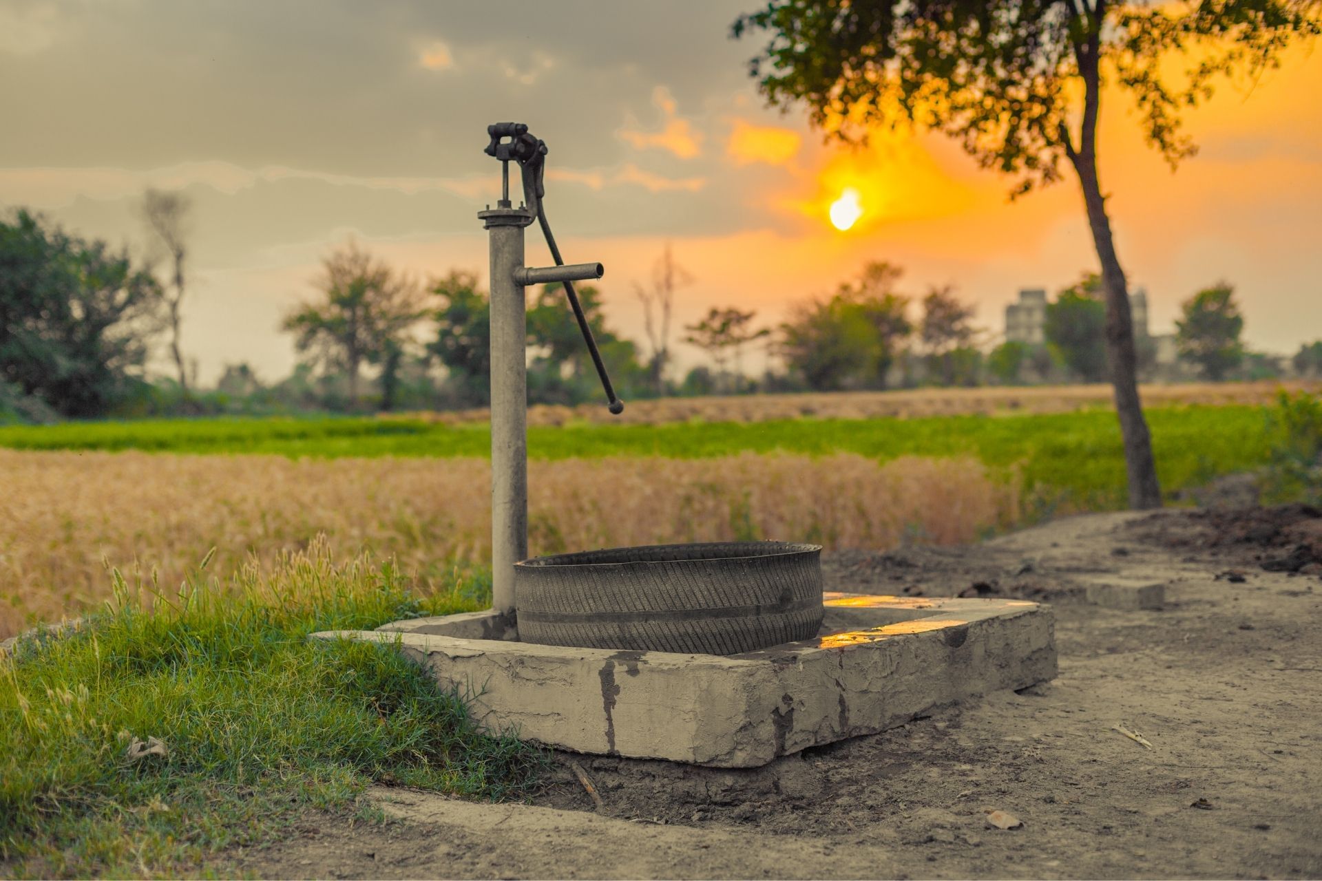 Manual water pump in a rural field at sunset, representing a groundwater source potentially used for monitoring water levels or detecting contaminants in agricultural areas.