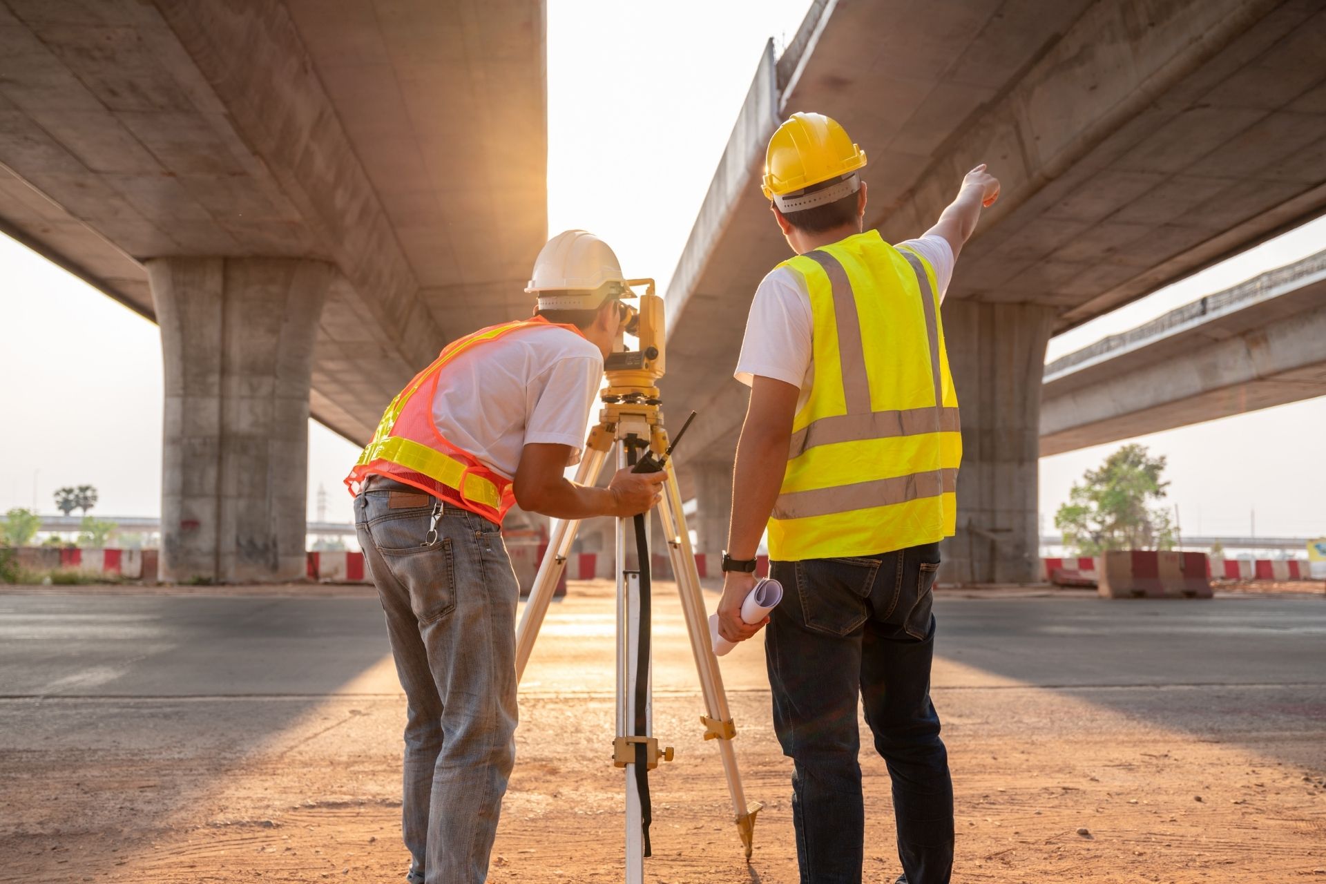 two construction workers standing under an overpass