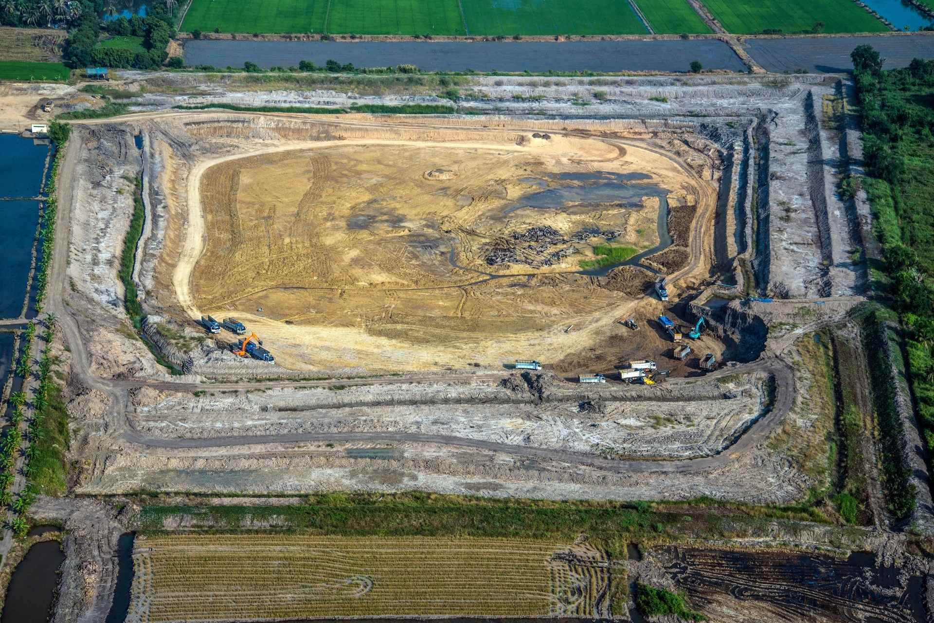 Aerial view of a contaminated land audit site with excavators and trucks clearing soil, surrounded by green farmland.
