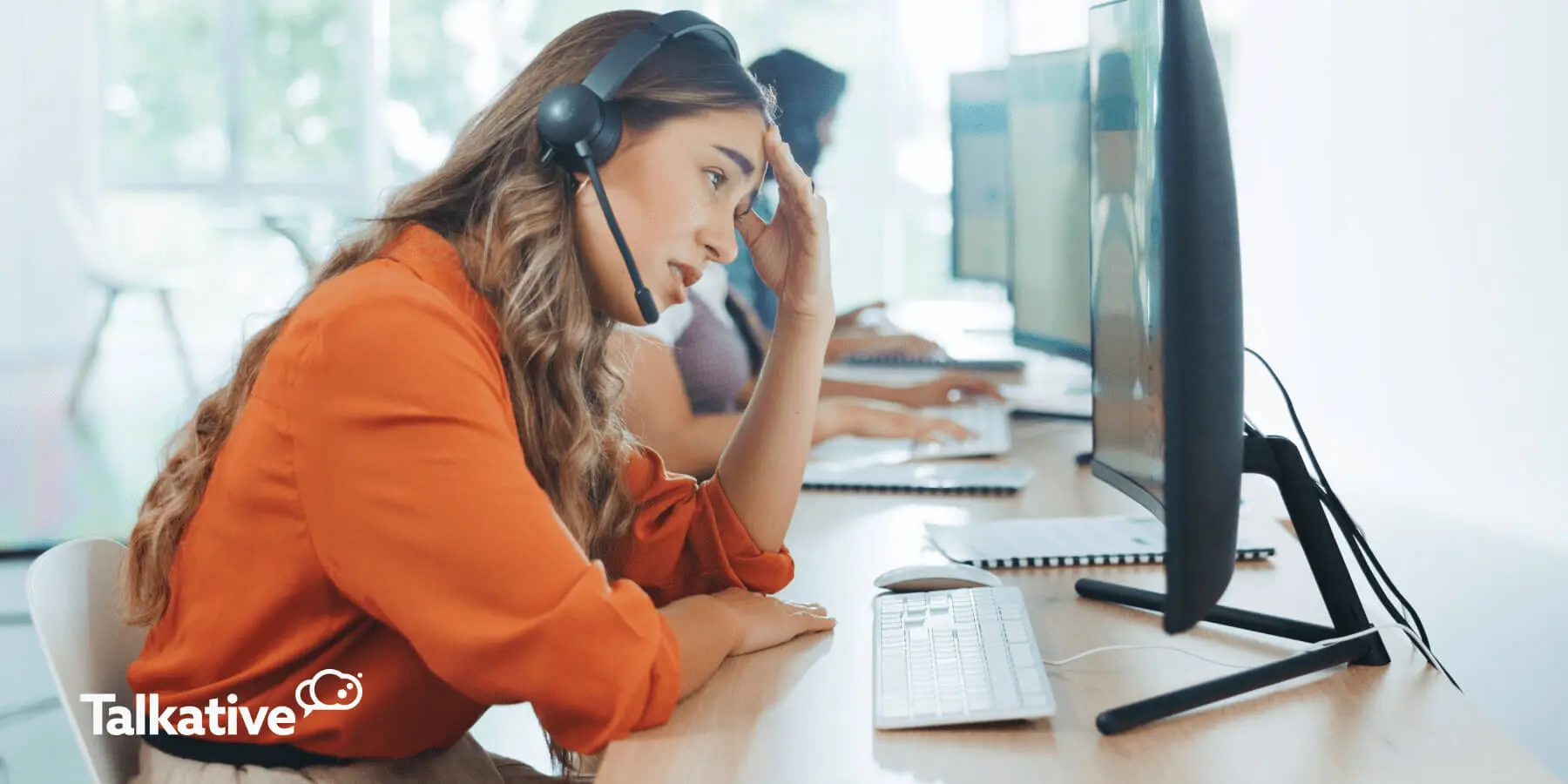 tired-looking contact centre agent sat at her desk in front of a computer with her head in her hand