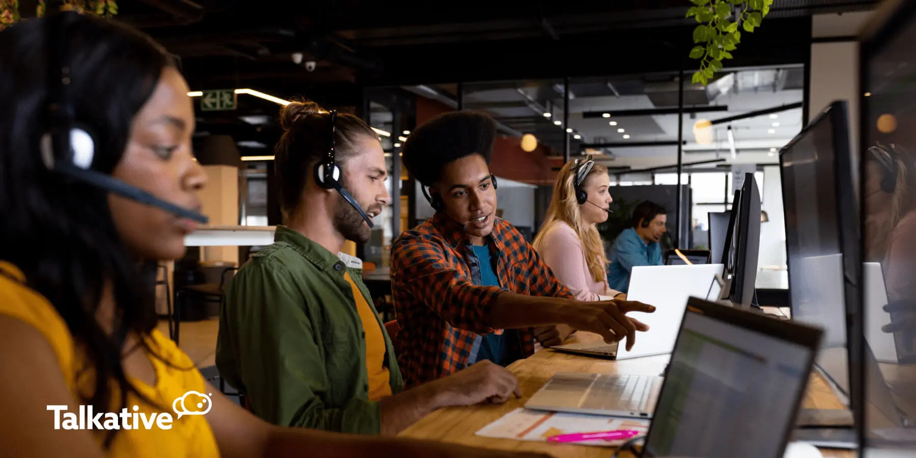 Image of contact centre agents wearing headsets and working at computers, with colleagues collaborating.