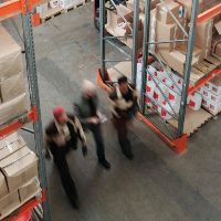 Three men walking in a warehouse with boxes.