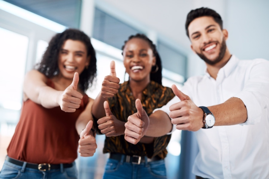 Three people giving thumbs up in front of a window.