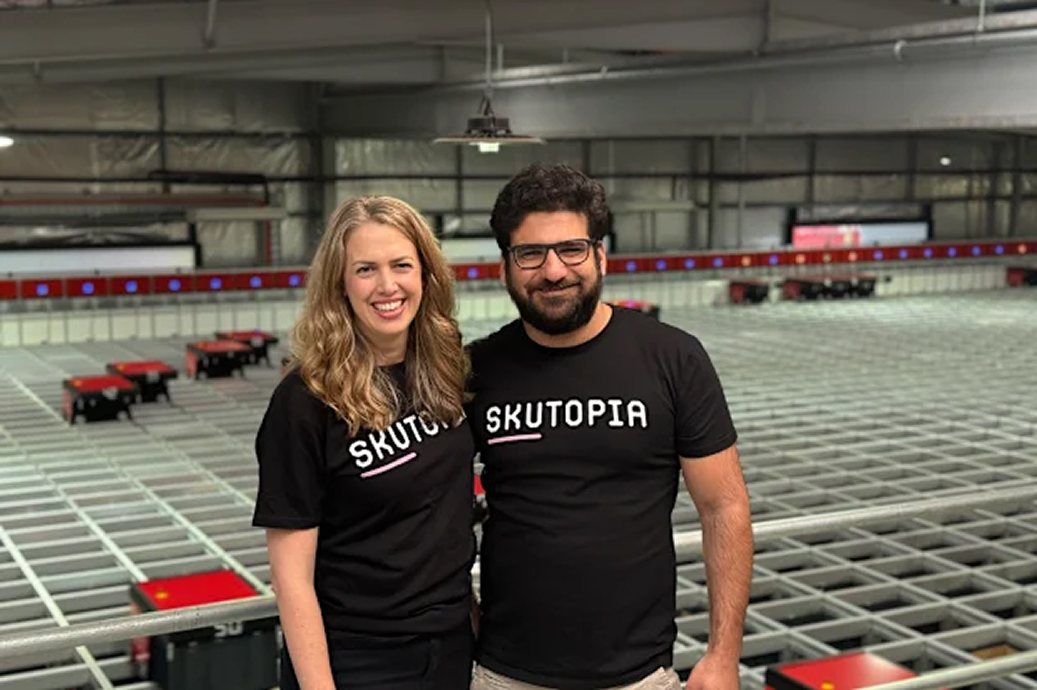 A man and woman stand in front of a Skutopia sign.