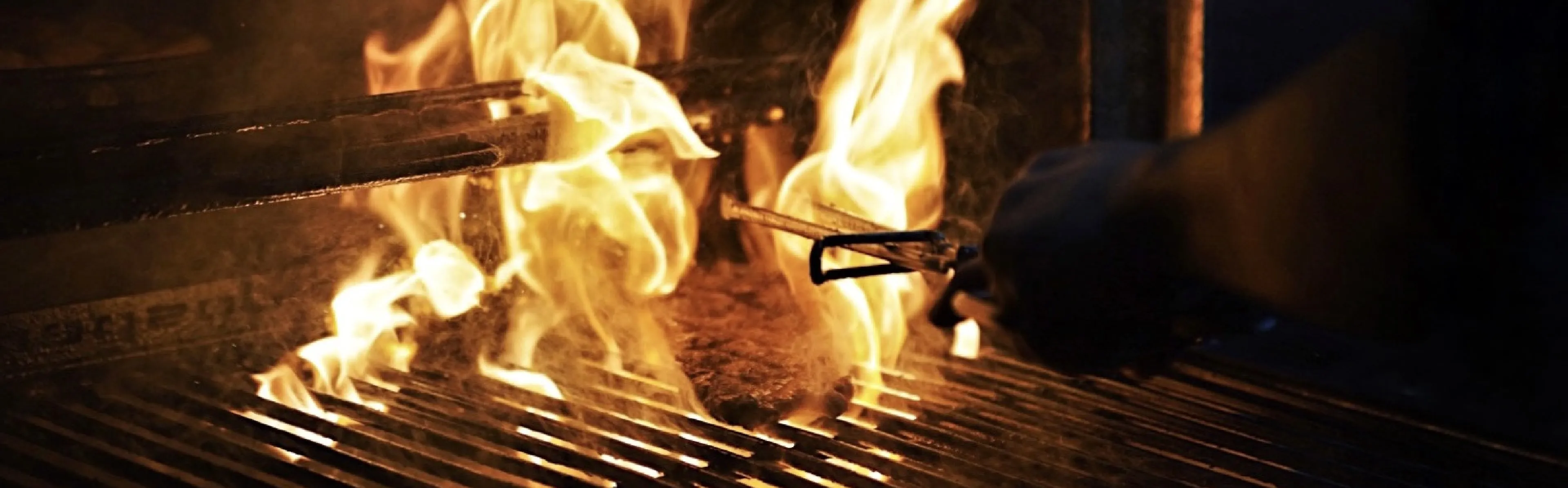 Charcoal Grilling Beef Steak with Flames over it an example of First Grill Grilled Food Singapore