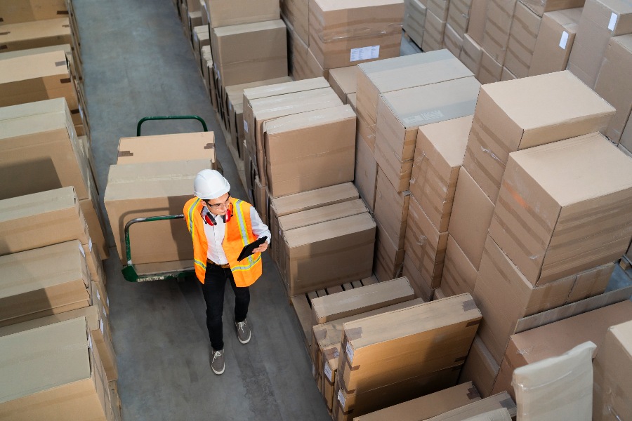 A man in a yellow vest is standing in front of a stack of brown boxes.